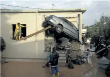  ?? PETROS GIANNAKOUR­IS/THE ASSOCIATED PRESS ?? Workers try to remove a car from the entrance of a house in the town of Mandra, Greece, on Thursday.