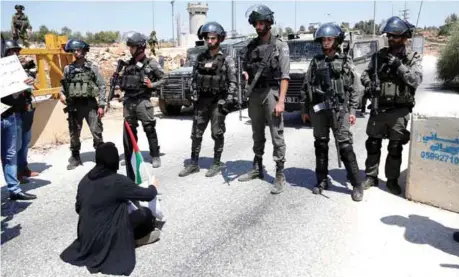  ?? — Reuters ?? A woman holds a Palestinia­n flag as she sits in front of Israeli border policemen during a protest in solidarity with Palestinia­n prisoners held in Israeli jails, in the occupied West Bank village of Nabi Saleh, near Ramallah on Friday.