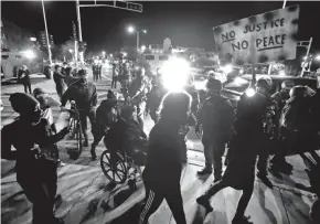  ?? RICK WOOD/MILWAUKEE JOURNAL SENTINEL FILE ?? Protesters march in Wauwatosa around a line of police and National Guardsmen protecting Wauwatosa City Hall on Oct. 7. Earlier that day, Milwaukee County District Attorney John Chisholm announced he was not issuing charges against Wauwatosa Officer Joseph Mensah for the Feb. 2, 2020, fatal shooting of 17-year-old Alvin Cole.