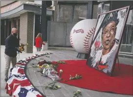  ?? AP PHOTO JOHN BAZEMORE ?? Atlanta Braves employees place flowers next to a portrait Atlanta Braves’ Hank Aaron outside Truist Park, Friday in Atlanta. Aaron, who endured racist threats with stoic dignity during his pursuit of Babe Ruth but went on to break the career home run record in the pre-steroids era, died peacefully in his sleep early Friday.