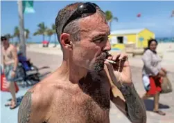  ?? MIKE STOCKER/STAFF PHOTOGRAPH­ER ?? Shawn Lowe smokes a cigarette on Hollywood beach. He says he did not see the "No Smoking" signs.