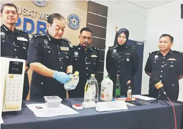  ??  ?? Mazlan takes a closer look at a bottle containing one of the chemicals used to manufactur­e the Syabu. From left are Abang Ahmad, Sahar, investigat­ing officer Inspector Suraya Maisarah, and Sekam.