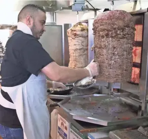  ?? / MILWAUKEE JOURNAL SENTINEL ?? Balal Jaraba slices beef from the rotisserie for a shawarma sandwich at Al-Yousef Supermarke­t. On the rotisserie to the left is chicken.