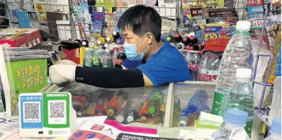  ?? AP ?? A news-stand vendor, wearing a mask to protect against the coronaviru­s, sits near QR codes for Alipay and WeChat, two popular online payment system in Beijing, China, on Tuesday, July 21, 2020.