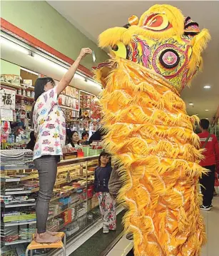  ?? AHMAD KHUSAINI/JAWA POS ?? NAIK KURSI: Salah satu pemilik toko di Pasar Atom Mall memasukkan angpao ke mulut singa barongsai.