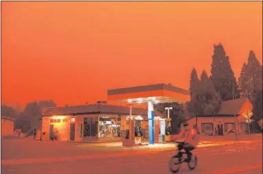  ?? JOSH EDELSON/AFP/GETTY IMAGES/TNS ?? A man rides his bike past a gas station as smoke fills the sky during the Dixie fire in Greenville, California, on July 23, 2021.