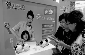  ?? AQING / FOR CHINA DAILY ?? Two Chinese women stand before a billboard advertisin­g Nanjing-based Tuniu.com while reviewing tourism informatio­n with their smartphone­s.