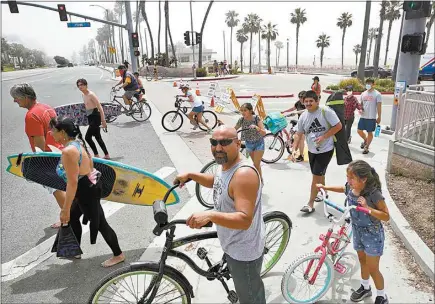  ?? MARCIO JOSE SANCHEZ / AP ?? People wait to cross Pacific Coast Highway on Sunday in Huntington Beach. A lingering heat wave lured people to California beaches, rivers and trails again Sunday, prompting warnings from officials that defiance of stay-at-home orders could reverse progress and bring the coronaviru­s surging back.