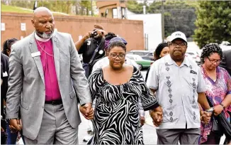  ?? HYOSUB SHIN / HSHIN@AJC.COM ?? Tamara Cotman, who was convicted in the Atlanta Public Schools test-cheating case, holds hands with Marietta Councilman Reggie Copeland (left) and the Rev. Timothy McDonald (third from left) as she turns herself in at the Fulton County Jail in Atlanta on Tuesday.