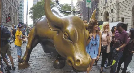  ?? (Reuters) ?? PEOPLE POSE next to the Wall Street Bull in Manhattan’s financial district.