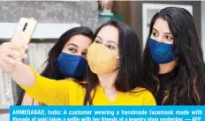  ??  ?? AHMEDABAD, India: A customer wearing a handmade facemask made with threads of gold takes a selfie with her friends at a jewelry shop yesterday. — AFP