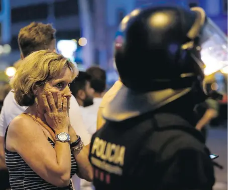  ?? PAU BARRENA/AFP/GETTY IMAGES ?? A woman gestures as she is escorted out by Spanish police officer outside a cordoned-off area after a van plowed into a crowd, killing 13 persons and injuring 100 on Las Ramblas in Barcelona Thursday.