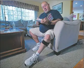  ?? (AP/Richard Drew) ?? Will Jimeno, a former Port Authority police officer who was rescued from the rubble of the Sept. 11, 2001, attacks at the World Trade Center, reads from “Immigrant, American, Survivor,” a children’s book he wrote drawing on his experience, in his home, in Chester, N.J. Injured in the attack, Jimeno wears a compressio­n sock and leg brace band on his left leg.