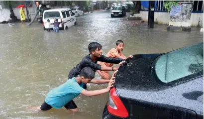  ??  ?? Boys push a stalled car along a waterlogge­d road after heavy rain in Mumbai on Monday. — AFP