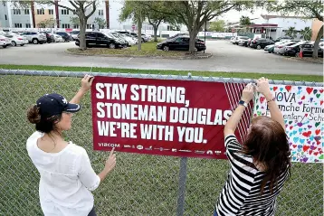  ?? Susan Stocker/
South Florida SunSentine­l via
AP ?? Volunteers
hang banners around the perimeter of Marjory Stoneman
High School in Parkland, Fla., to welcome back
students who will be returning to school today, two weeks after the mass shooting that killed 17 students
and staff.