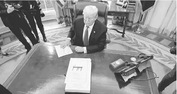  ??  ?? Trump sits at his desk as reporters exit after he signed sweeping tax overhaul legislatio­n into law in the Oval Office at the White House in Washington, US. — Reuters photo