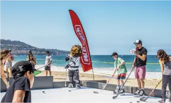  ??  ?? Le guru de l’entraîneme­nt Jeremy Rupke (avec le mégaphone), guide des jeunes qui essaient la surface synthétiqu­e de HockeyShot sur une plage en Californie. - Gracieuset­é