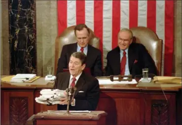  ?? BOB DAUGHERTY — THE ASSOCIATED PRESS FILE ?? President Ronald Reagan holding up 14-pound continuing resolution for the budget, part of a total package weighing 43-pounds, which the president said was two months late from Congress, during his State of the Union address on Capitol Hill in Washington. Vice President George H.W. Bush, left, and House Speaker James Wright of Texas listen behind him.