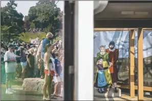  ?? (AP/David Goldman) ?? A crowd is reflected in the window of a ticket booth next to a cutout, right, of Pilgrims as they wait for the Mayflower II, a replica of the original Mayflower ship that brought the Pilgrims to America 400 year ago, to sail into Plymouth, Mass. The 102 passengers aboard the Mayflower, equal numbers “saints” and “strangers,” didn’t cross the Atlantic to establish a democratic society. When they set sail from Plymouth, England, on Sept. 16, 1620, they were escaping religious persecutio­n and looking for a place where they could prosper.