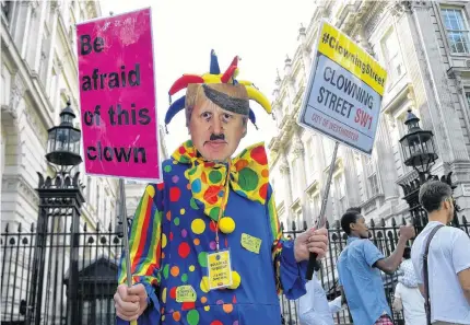  ??  ?? An anti-brexit protester wearing a clown costume and a defaced mask depicting British Prime Minister Boris Johnson holds placards in Westminste­r in London Thursday. •