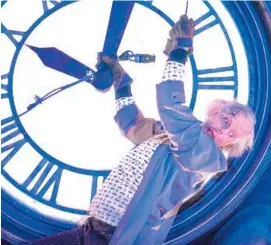  ?? Doc Brown (Christophe­r Lloyd) hangs on to the Hill Valley (Universal backlot) clock. Photo from Universal ??