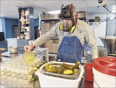  ??  ?? Owner Tim Bibens wears a gas mask as he adds pickling brine to glass jars as he makes pickles infused with horseradis­h in the Galway plant.