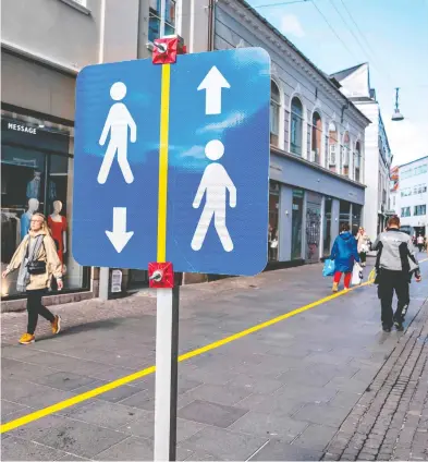  ?? HENNING BAGGER / RITZAU SCANPIX / AFP VIA GETTY IMAGES ?? A painted yellow stripe divides a pedestrian street in Aalborg, Denmark, in order to help people to comply with the social distance guidelines during the pandemic. Some distancing restrictio­ns were loosened in Denmark Monday.