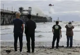  ?? ?? People watch a helicopter drop water as crews fight a fire burning at the end of the Oceanside Municipal Pier in Oceanside, California on Thursday. Photograph: Hayne Palmour IV/ Rex/Shuttersto­ck