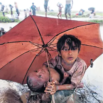  ??  ?? A Rohingya girl holds an umbrella over her little sister as they make their way across Burma’s border to enter Bangladesh