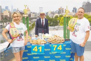  ?? JOHN MINCHILLO/AP ?? Competitiv­e eaters Miki Sudo, left, and Joey Chestnut, right, pose for photograph­s with host George Shea, center, after a weigh-in before the Nathan’s Famous July Fourth hot dog eating contest Friday in the Brooklyn borough of New York City. The weigh-in was held in a private, socially distanced ceremony in the Williamsbu­rg neighborho­od because of concerns about the coronaviru­s outbreak.