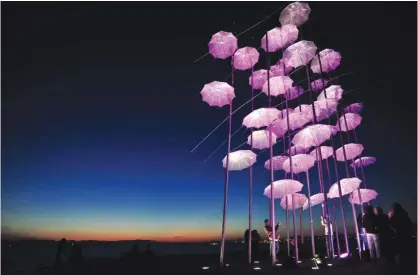  ??  ?? THESSALONI­KI, Central Macedonia, Greece: People stand in front of an artwork illuminate­d in pink, “Umbrellas” by Greek sculptor George Zongolopou­los, part of a campaign to raise awareness and promote prevention and treatment of breast cancer, along the...