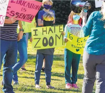  ?? EDUARDO CONTRERAS U-T ?? Parents and students hold signs at a rally outside the SDUSD Board of Education Headquarte­rs on Tuesday in San Diego. School district officials announced that they are targeting April 12 for reopening schools.