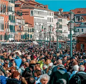  ??  ?? Tourists jostle for space as they walk beside typical Venetian buildings near St Mark’s Square.