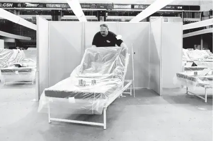  ?? RICH PEDRONCELL­I/AP ?? Robert Reynolds, of the California Department of Forestry and Fire Protection, moves a bed into position as work is performed to turn Sacramento’s former Sleep Train Arena into a 400-bed emergency field hospital to help deal with the coronaviru­s outbreak in April.