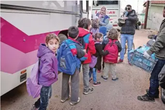  ??  ?? Children board a bus to get to school as volunteer holds a crate with sandwiches prepared in camps ‘cafe Rits’.