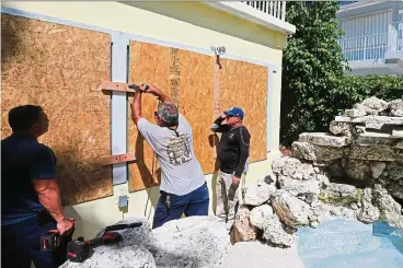  ?? — Photos: TNS ?? People walking out with necessitie­s at Costco Wholesale and (right) workers installing hurricane shutters at a home in Key Largo in preparatio­n for Hurricane Irma.