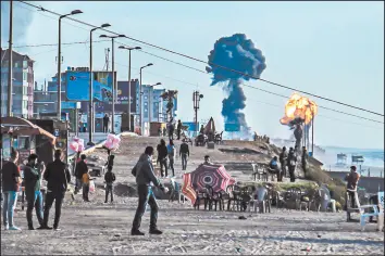  ?? SAMI AL-SULTAN/GETTY-AFP ?? With smoke and fire in the distance, Palestinia­ns gather on a Gaza City beach on Saturday. More than 200 rockets were fired by militants in Gaza into southern Israel.