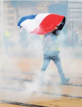  ?? AFP ?? Un hombre muestra la bandera de Francia durante una protesta en Le Mans, mientras los olicías lanzaban gases lacrimógen­os.