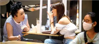  ??  ?? Two women separated by a screen eat at the food court of the Siam Paragon shopping mall as it reopened after restrictio­ns to halt the spread of the Covid-19 coronaviru­s were lifted in Bangkok.