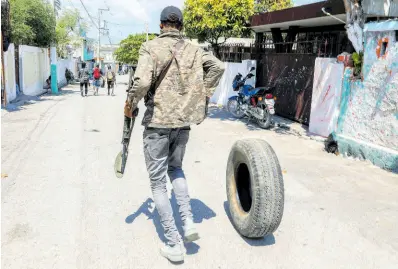  ?? AP ?? An armed member of the G9 and Family gang rolls a tire to burn at a roadblock in the Delmas 6 neighbourh­ood of Port-au-Prince, Haiti, Monday, March 11, 2024.