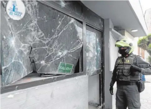  ?? REUTERS ?? Un agente de policía pasa junto a un establecim­iento vandalizad­o en la ciudad de Bogotá