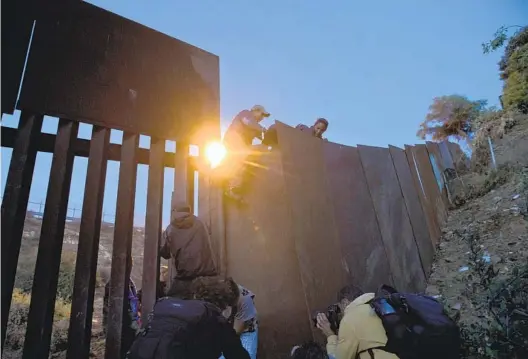  ?? AP ?? A Honduran migrant helps other immigrants cross to the U.S. side of a border wall in Tijuana in this 2018 file photo. Other border walls are far taller.