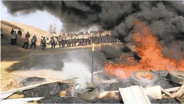  ?? MIKE MCCLEARY/THE BISMARCK TRIBUNE VIAASSOCIA­TED PRESS ?? Tires burn as armed soldiers and law enforcemen­t officers stand in formation Thursday to force Dakota Access pipeline protesters off private land where they had camped to block constructi­on.