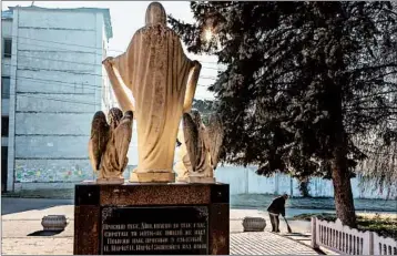  ?? OKSANA PARAFENIUK/WASHINGTON POST ?? A woman sweeps leaves near a statue of the Virgin Mary and four angels where a Vladimir Lenin monument used to be.