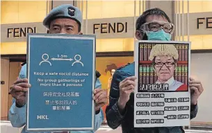  ?? VINCENT YU THE ASSOCIATED PRESS ?? A security guard holding a safety notice stands next to a pro-democracy protester at a shopping mall in Hong Kong on Wednesday. Social distancing rules prohibit public gatherings of over four.