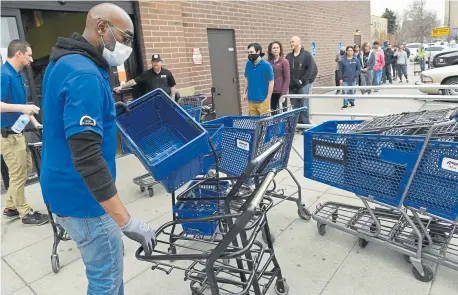  ?? Helen H. Richardson, The Denver Post ?? An employee who is known as Upgrade organizes and sanitizes shopping carts before giving them to customers waiting in line to shop at Argonaut Liquors on Monday in Denver. People rushed to liquor stores after Mayor Michael Hancock’s stay-at-home order, fearing the stores would close Tuesday evening.