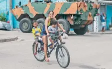  ??  ?? Una mujer transporta dos niños en bicicleta mientras militares de las Fuerzas Armadas brasileñas realizan un operativo, en Río de Janeiro.