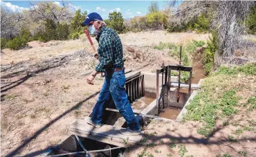  ?? EDDIE MOORE/JOURNAL ?? Mayordomo Narciso Quintana, 82, walks over a gate on an acequia in Nambe in April 2020. The state’s capital outlay system for funding road, bridge, dam and water systems improvemen­ts has come under scrutiny in recent years for both secrecy and inefficien­cy.