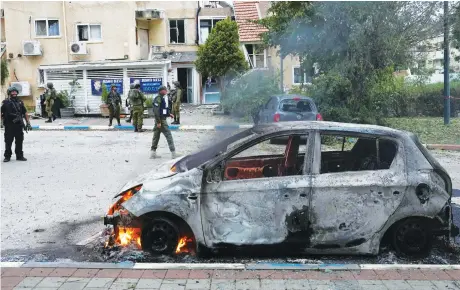  ?? Reuters ?? Israeli troops in Kiryat Shmona stand next to a burning car at the impact site of a rocket that was fired from Lebanon.