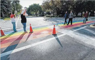  ?? GARY YOKOYAMA THE HAMILTON SPECTATOR ?? LGBTQ supporters Christina Mulder and Chris Farias greet pedestrian­s crossing the rainbow crosswalk at the Sterling Street entrance to McMaster University on Friday morning after white paint was spilled on it.